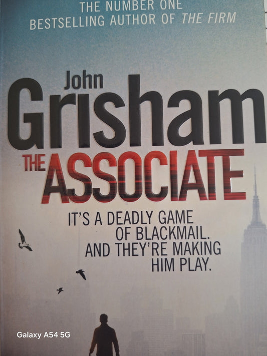 Used John Grisham The Associate book cover featuring a skyline and suspenseful themes